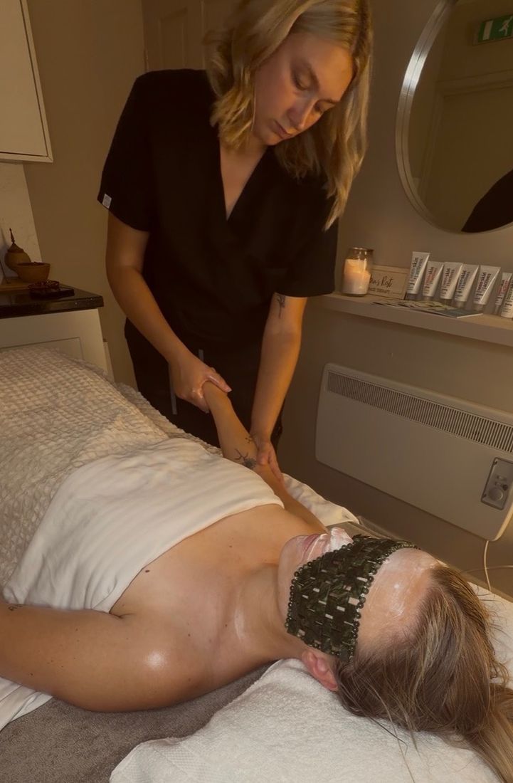 Antonia massaging a client's arm during a facial, with a jade eye mask on